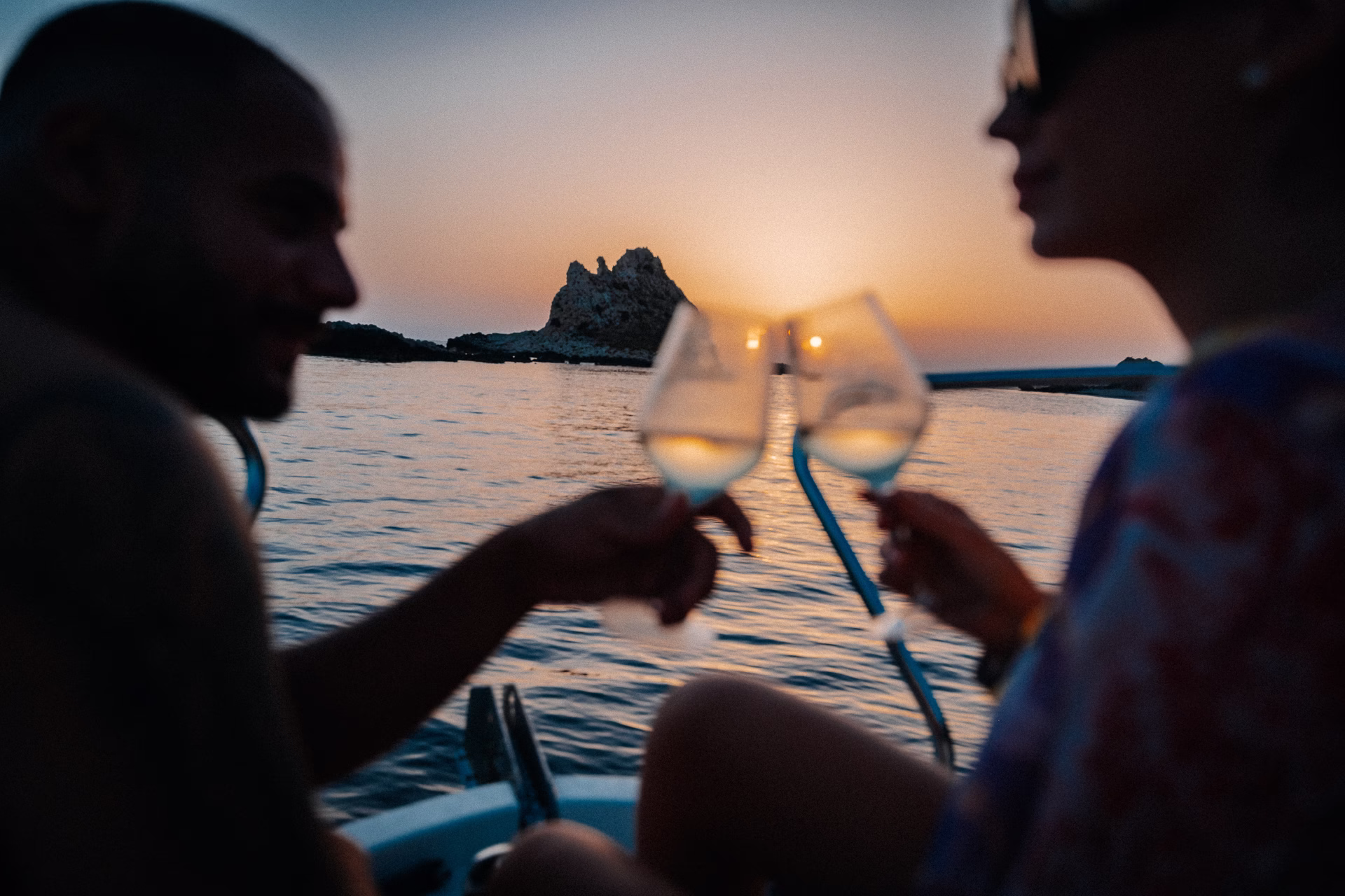 Coppia su una barca a Favignana che brinda con calici di vino bianco al tramonto, fotografia di Andrea Ventura