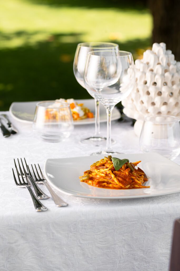 Tavola elegante all’aperto con piatto di pasta e calici di vino – food photography VA Photo