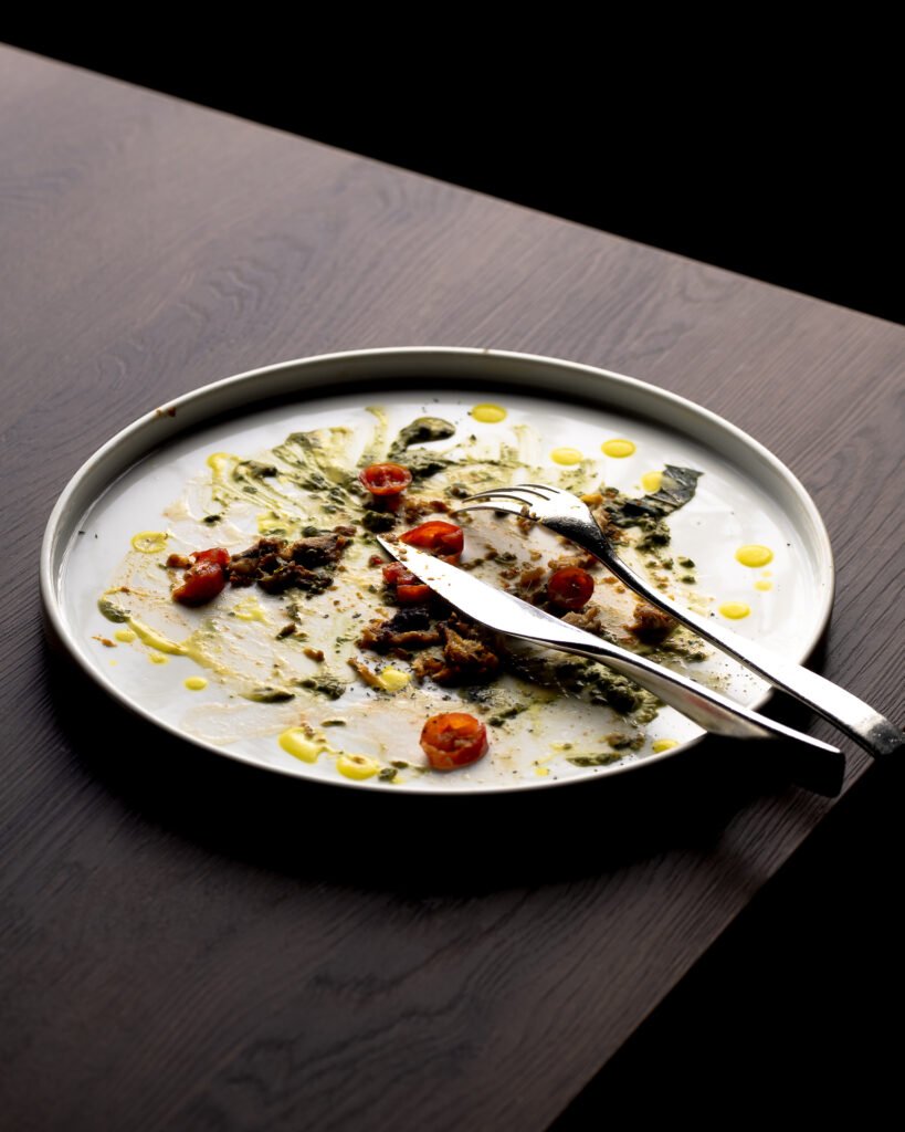 Piatto appena terminato con posate su tavolo in legno scuro, fotografia di Andrea Ventura