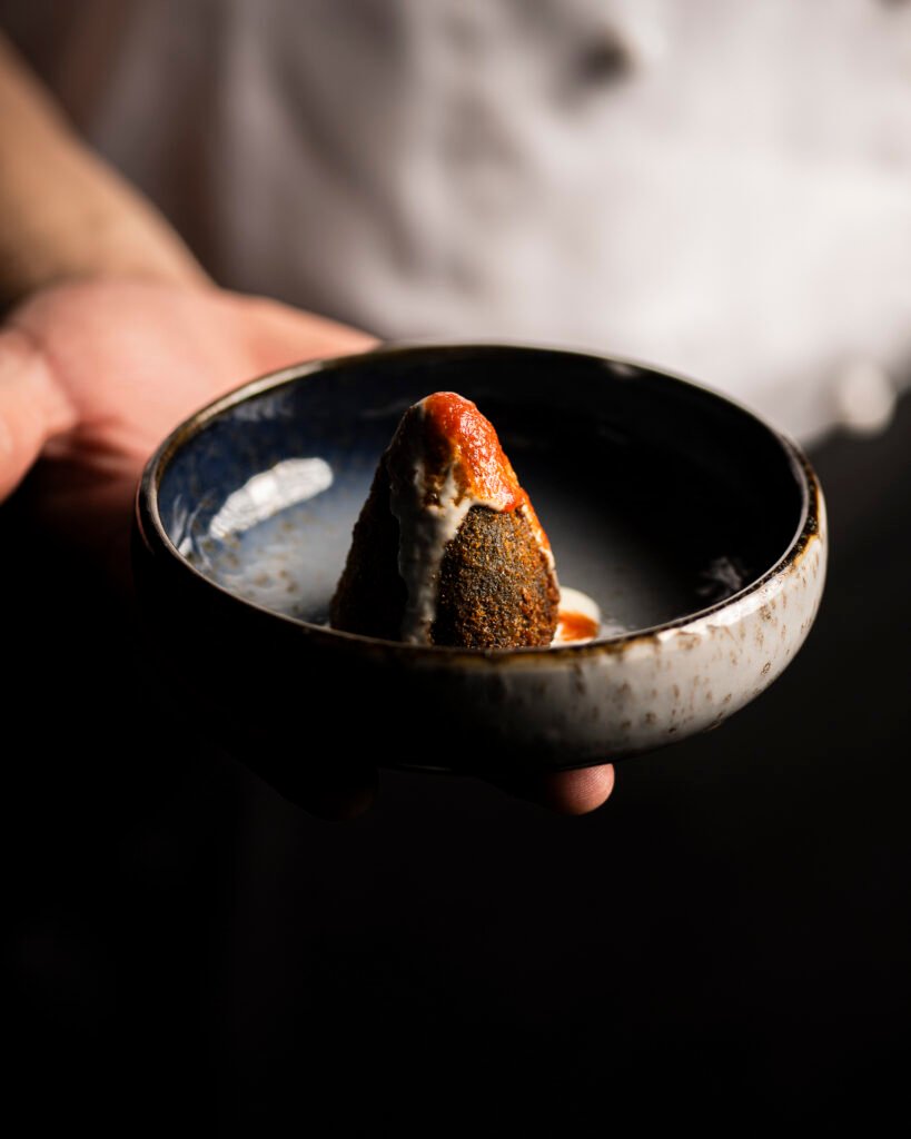 Mani dello chef che porgono una ciotola in ceramica con un fritto e salsa di pomodoro